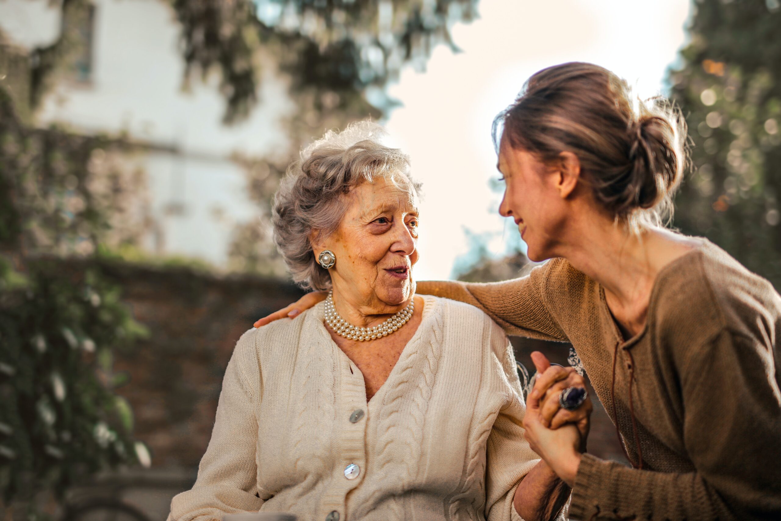 Smiling older woman shares a warm moment with a younger woman, highlighting a strong intergenerational bond in a serene outdoor setting.