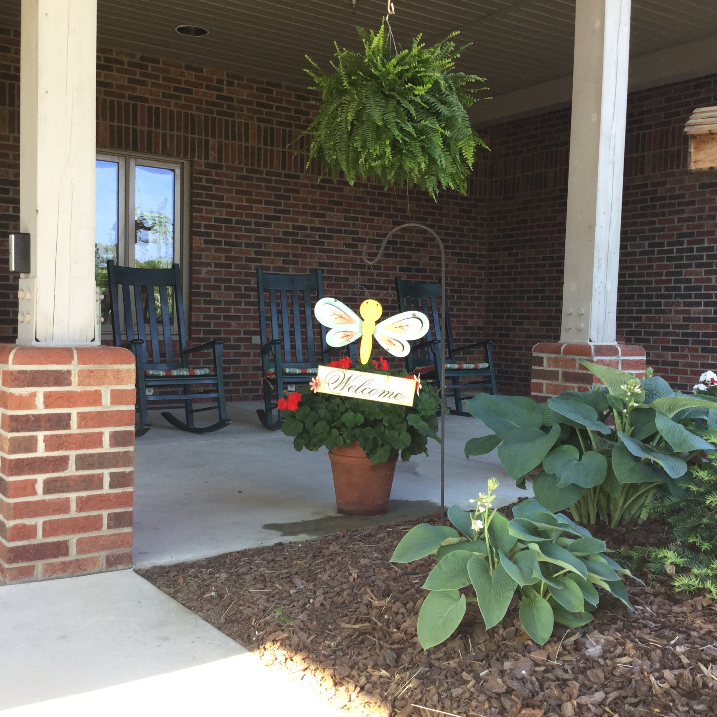 Welcoming porch with rocking chairs, a hanging fern, and a flowerpot featuring a cheerful "Welcome" sign adorned with a butterfly motif.