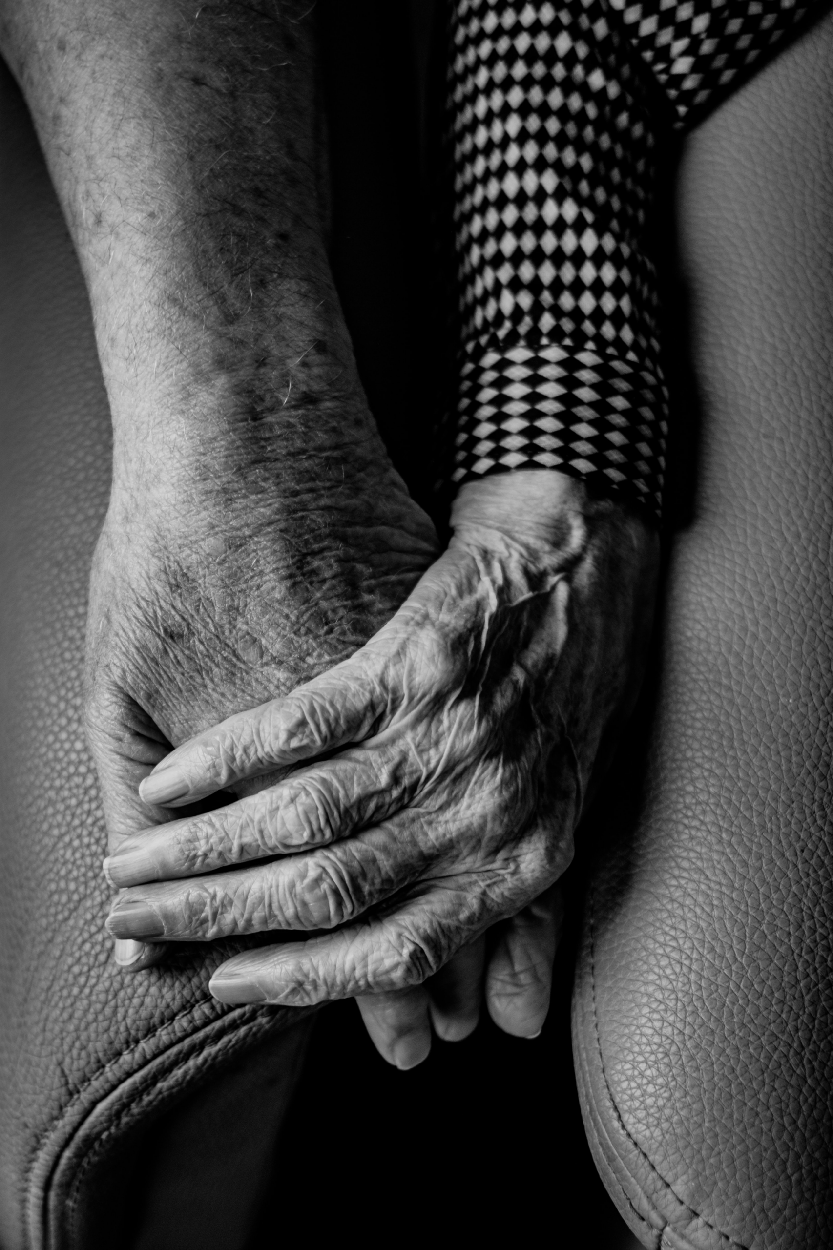 Two aged hands clasped together resting against a textured surface, symbolizing connection and intimacy in a moment of tenderness.
